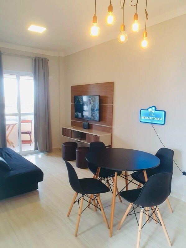 A modern living room with a flat-screen TV, a dining table with chairs, and a sofa.