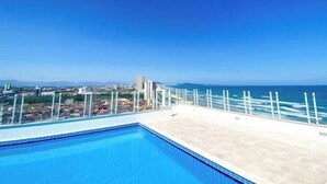 A rooftop pool with a clear view of the ocean and cityscape. - Pé na areia apto c vista mar e piscina (Praia Grande)