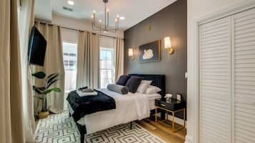 Une chambre moderne avec un lit, des tables de chevet, une télévision et une grande fenêtre avec des rideaux.