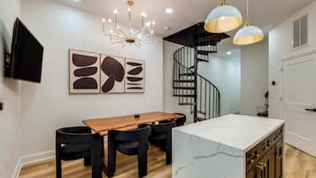 Une cuisine moderne avec une table à manger en bois, des chaises noires, un îlot en marbre, des luminaires suspendus et un escalier en colimaçon noir.