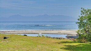 Paisatge costaner amb una platja, zona verda i muntanyes al fons.