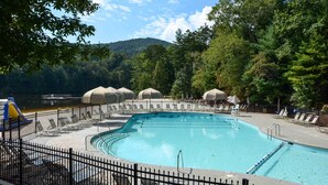 Une piscine entourée d’arbres, avec des chaises longues et des parasols, et offrant une vue sur un lac.
