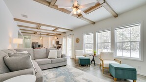 A modern living room with a grey sectional sofa, a white round coffee table, and a teal ottoman. There is a large window with a view of snow-covered trees. - Walk to Beach: Modern Retreat in Presque Isle! (Presque Isle)