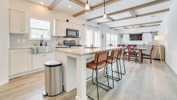 A modern kitchen with white cabinets, a stainless steel sink, a microwave, and a large island with bar stools. - Walk to Beach: Modern Retreat in Presque Isle! (Presque Isle)