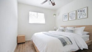 A bedroom with a bed, a ceiling fan, a window, and wall art.