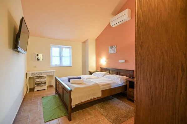 A bedroom with a bed, a desk, a mirror, and an air conditioning unit.