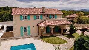 Una casa de dos pisos con piscina, un patio cubierto y vistas del paisaje circundante.