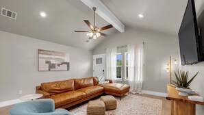 Un salon moderne avec un canapé d’angle en cuir marron, un fauteuil bleu, une petite table ronde et un ventilateur de plafond.