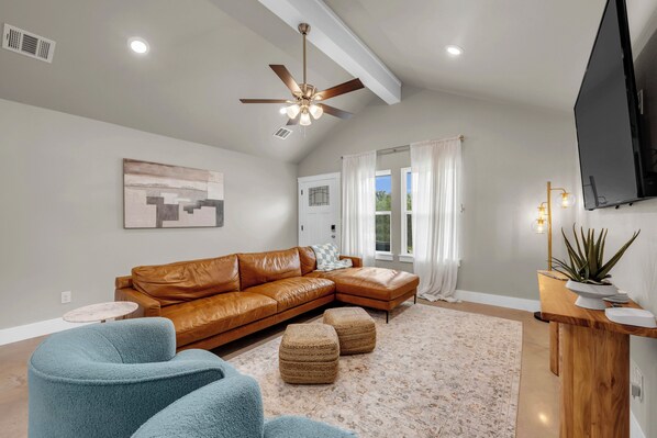 Un salon moderne avec un canapé d’angle en cuir marron, un fauteuil bleu, une petite table ronde et un ventilateur de plafond.