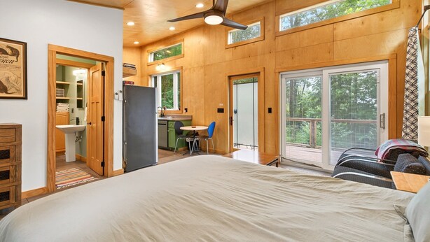 Un dormitorio con cama, ventilador de techo, escritorio con silla y vistas amplias por una ventana grande.