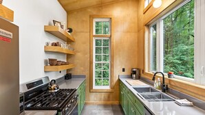 Una cocina moderna con estantes de madera, una ventana y vistas al verdor.