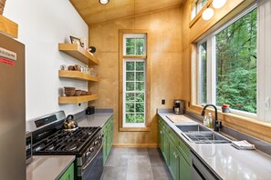 A modern kitchen with wooden shelves, a window, and a view of greenery.