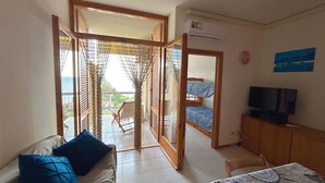A room with a sofa, a TV, a balcony with a view, and a wooden door. - Apartment Blue Sea with sea view (Talamone)