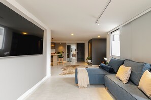 A modern living room with a sectional sofa, a flat-screen TV, and a dining area in the background. - Torre San Tomas (Medellín)