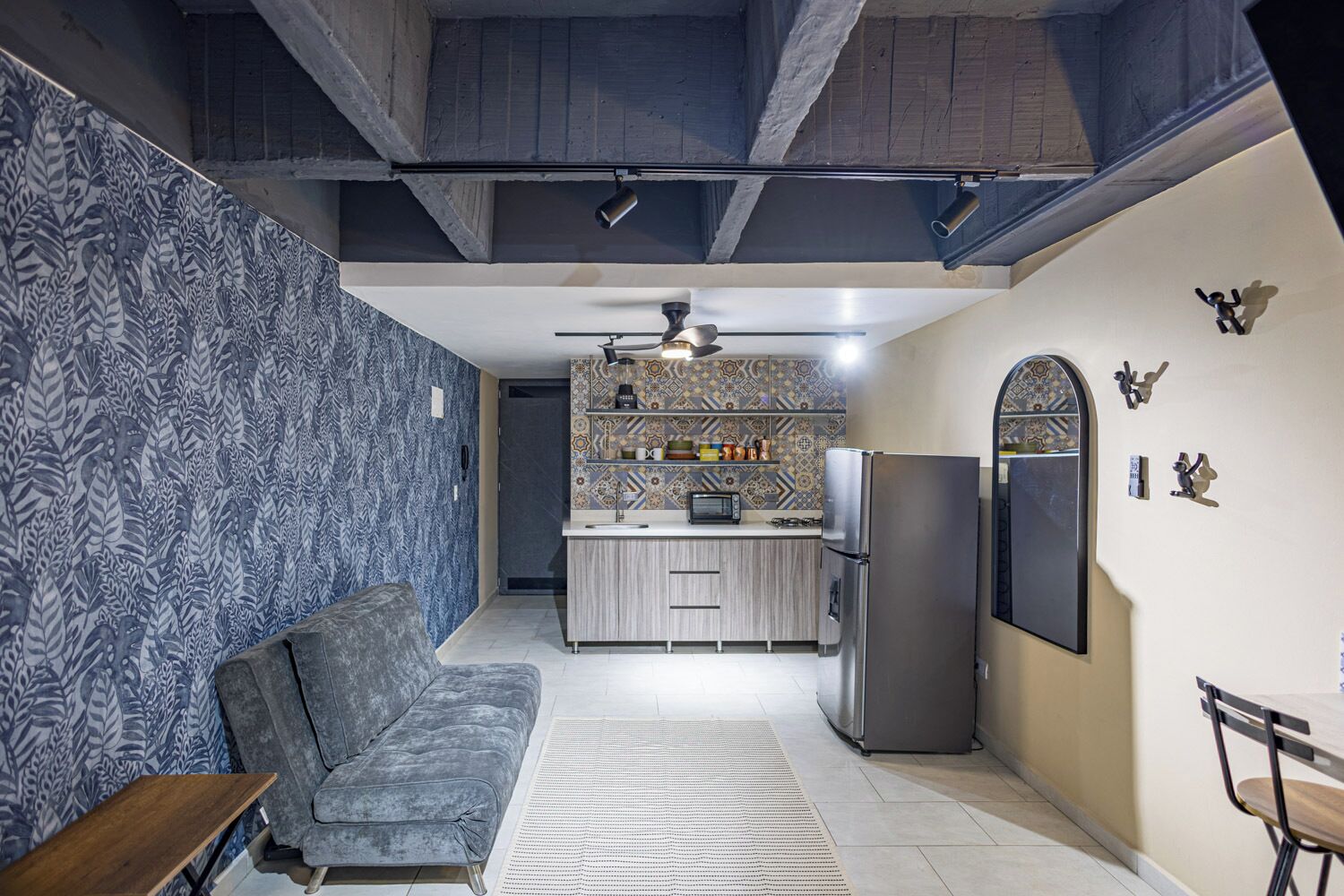 A compact living space with a kitchenette, a sofa, a refrigerator, and a ceiling fan.