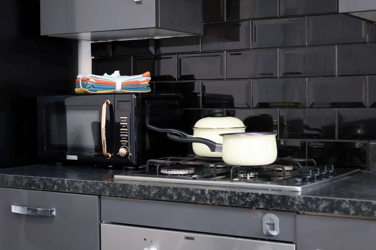 Una cucina con un forno a microonde nero, un fornello a gas e una pentola sul fuoco.