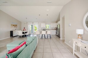 Amplia sala de estar con mesa y sillas de comedor, cocina equipada con electrodomésticos modernos y un gran ventanal que proporciona luz natural.