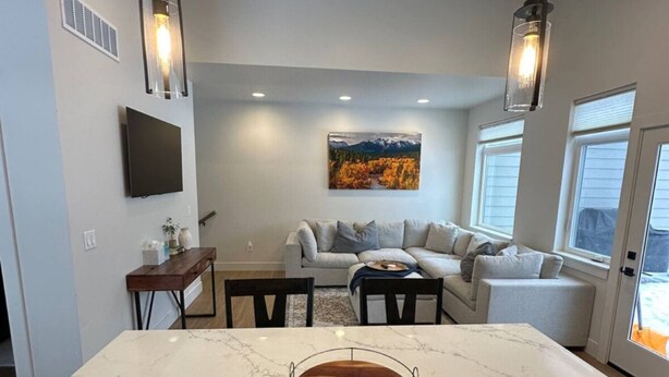 A modern kitchen with a marble island, recessed ceiling lights, a dining area with a sofa, and a large window.