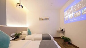 Une chambre d’hôtel avec deux lits, un écran de projection, une petite étagère avec quelques objets et une plante en pot.