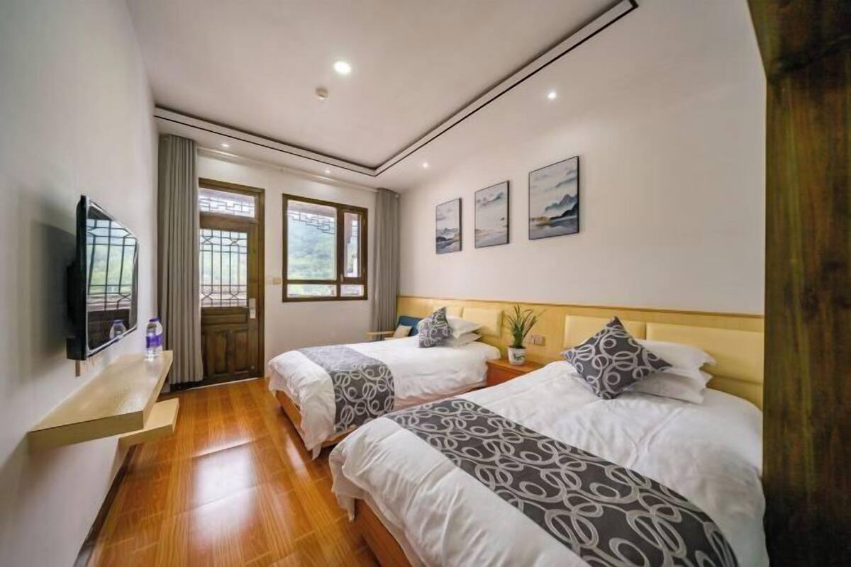 Ein Hotelzimmer mit zwei Betten, einem Fernseher, einem Fenster und Bildern an der Wand.