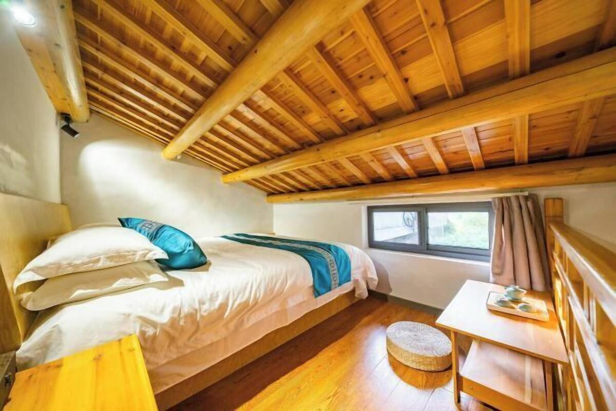 Ein Zimmer mit Holzboden, einem Bett mit Kissen, einem kleinen Tisch und einem Fenster.
