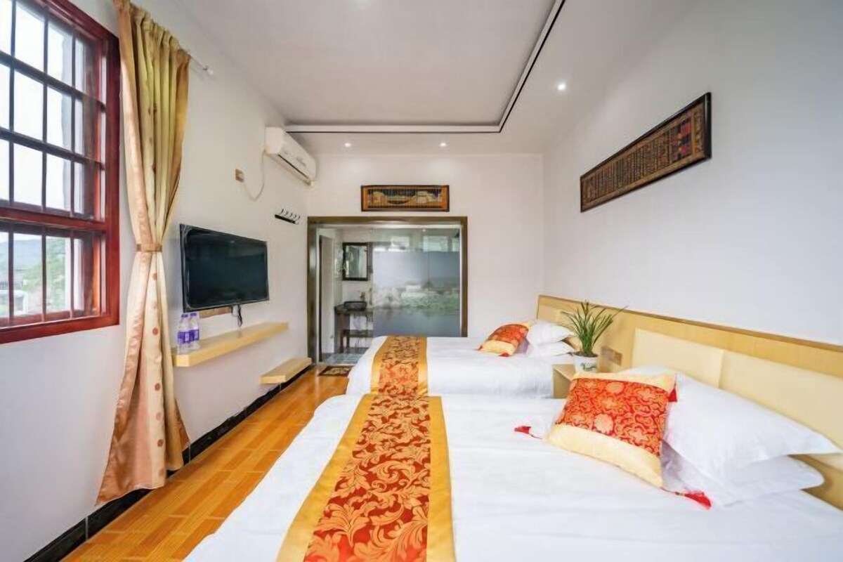 A hotel room with two beds, a TV, a window with curtains, and a door leading to a balcony.