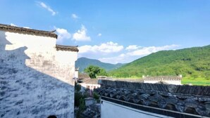 Un bâtiment traditionnel à la façade blanche et au toit recouvert de tuiles, qui offre une vue sur une vallée verdoyante et des montagnes.