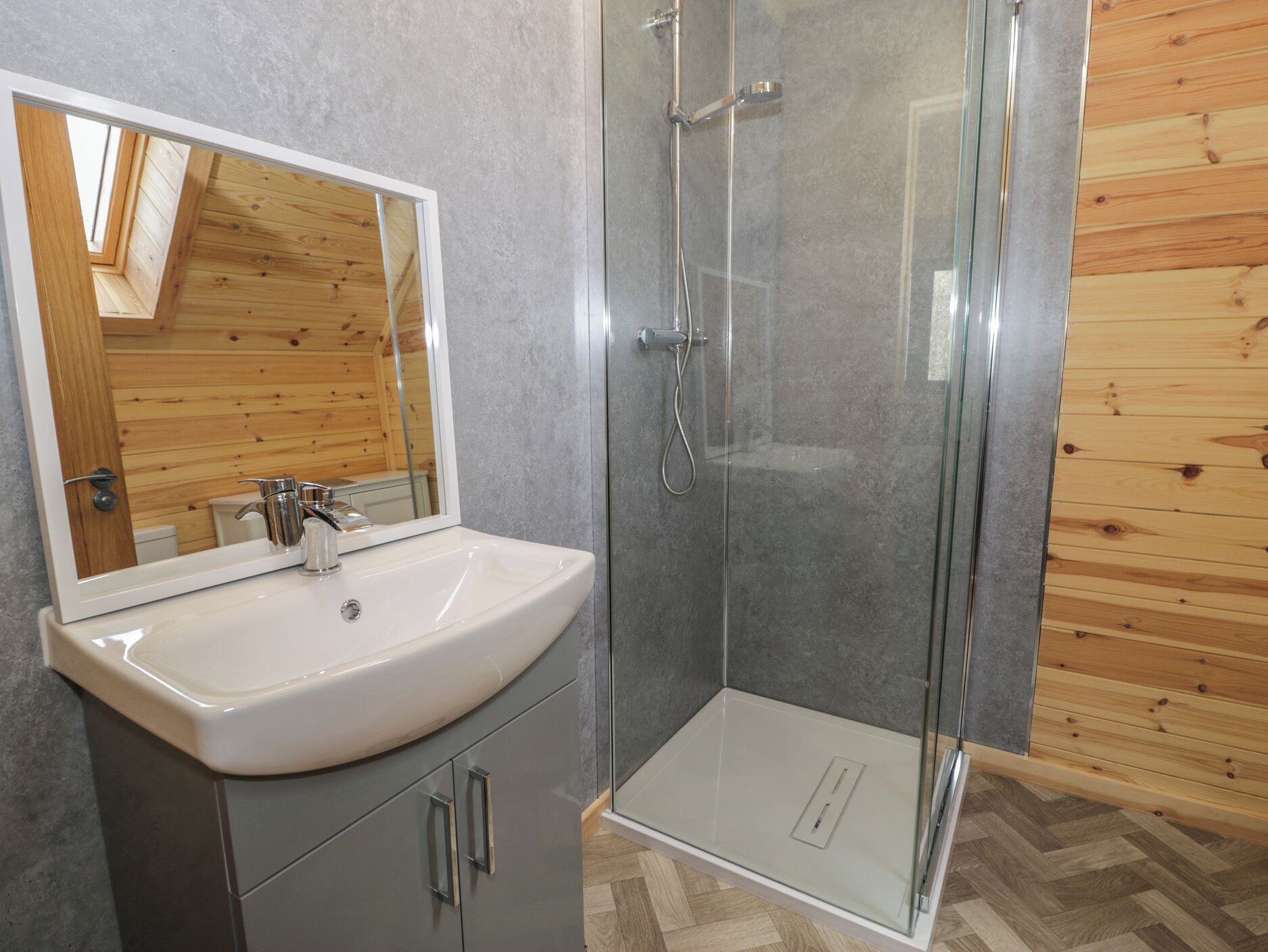 Un baño con ducha de vidrio, un lavamanos blanco y un espejo.