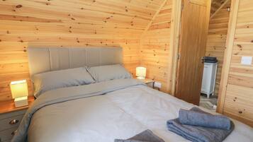 A cozy wooden cabin bedroom with a bed, bedside lamps, and neatly folded towels.