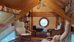 Une pièce mansardée chaleureuse avec des poutres en bois, une fenêtre ronde et une bibliothèque.