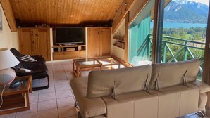 Un intérieur en bois avec un canapé, une télévision et un balcon offrant une vue sur la montagne.