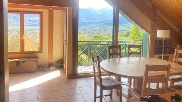 Un intérieur en bois comprenant une table à manger, des chaises et une vue sur un paysage montagneux, visible à travers de grandes fenêtres.