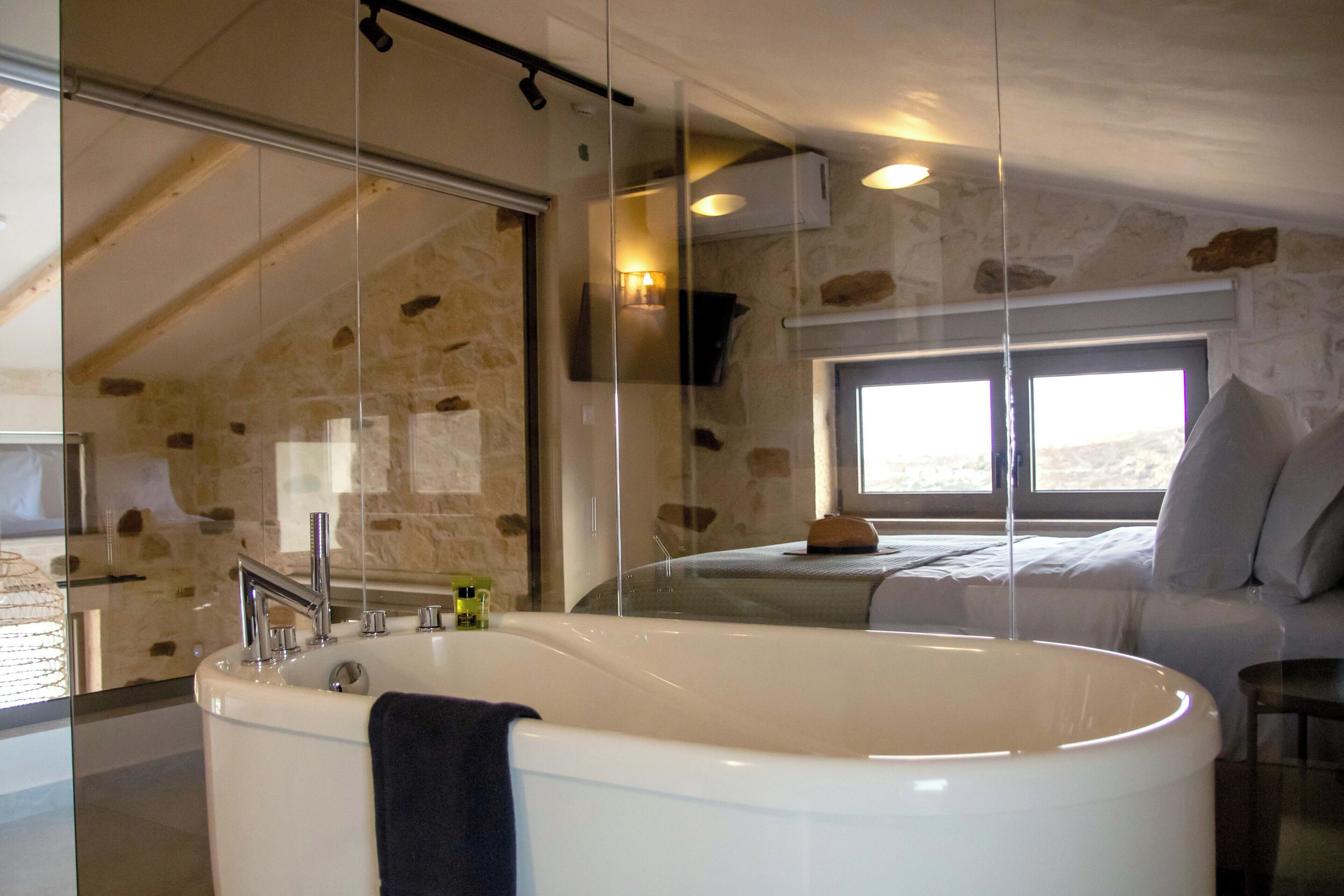 Une salle de bain moderne avec une baignoire sur pieds, une douche à l’italienne et un mur en pierre.