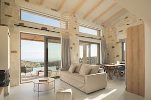 A spacious living area with a sofa, dining table, and chairs, large windows with a view, and a stone wall.