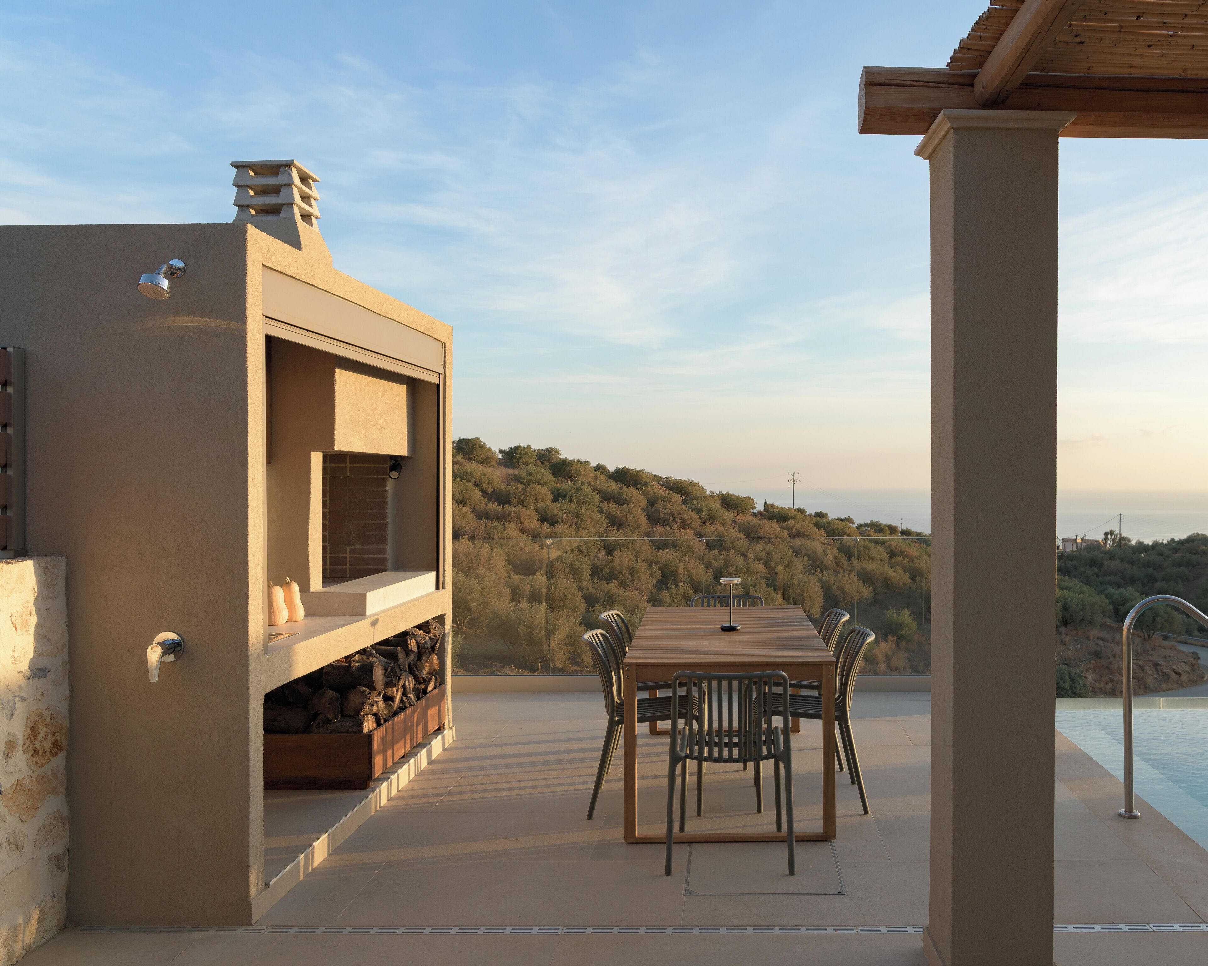 Une terrasse extérieure avec une table et des chaises, un barbecue intégré et une vue sur un paysage vallonné.