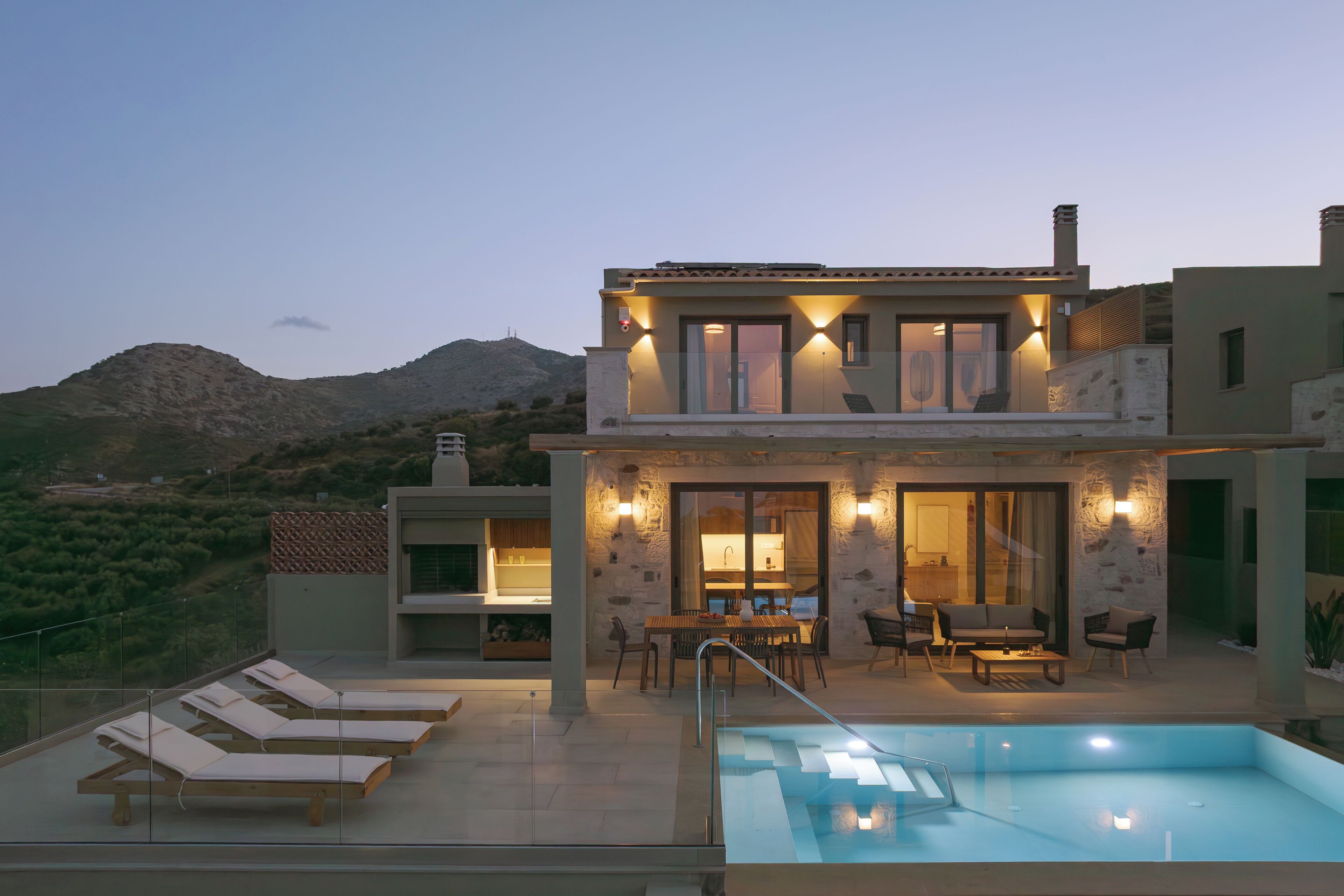 A modern two-story building with a pool, outdoor seating, and a view of the mountains.