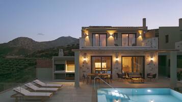 A modern two-story building with a pool, outdoor seating, and a view of the mountains.