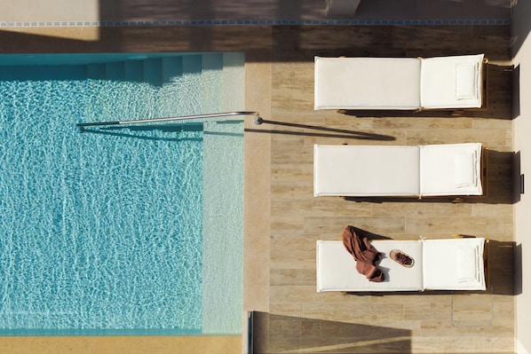 A rooftop pool with clear water, wooden deck, and two lounge chairs with towels.