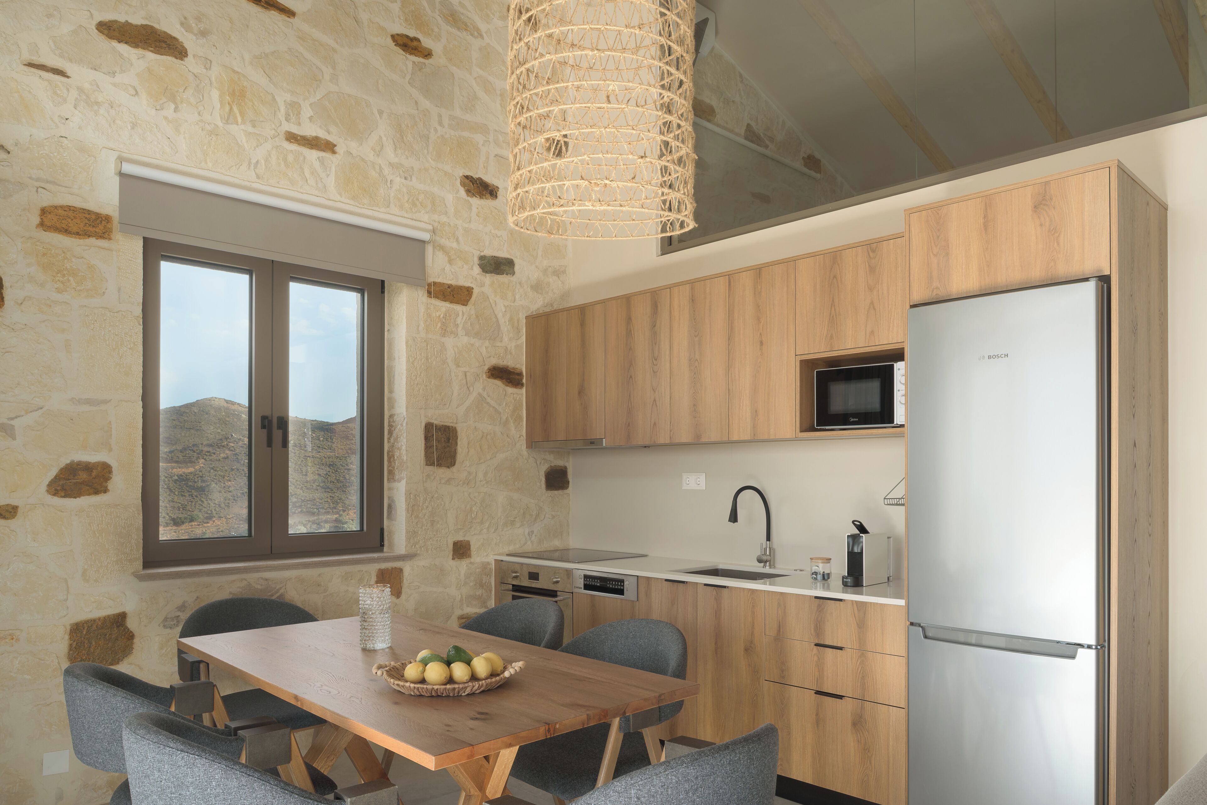 A modern kitchen with stone walls, wooden cabinets, a Bosch refrigerator, and a dining area with a table and chairs.