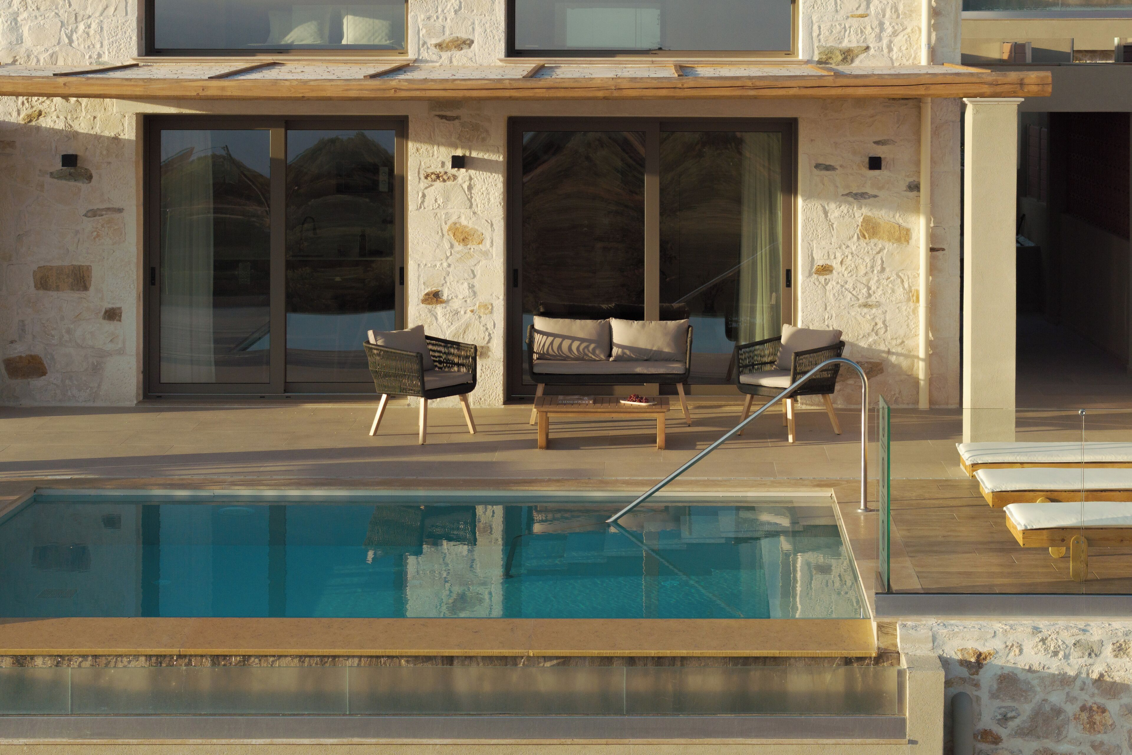 Une piscine avec des chaises longues, une entrée avec une porte vitrée et une façade en pierre.