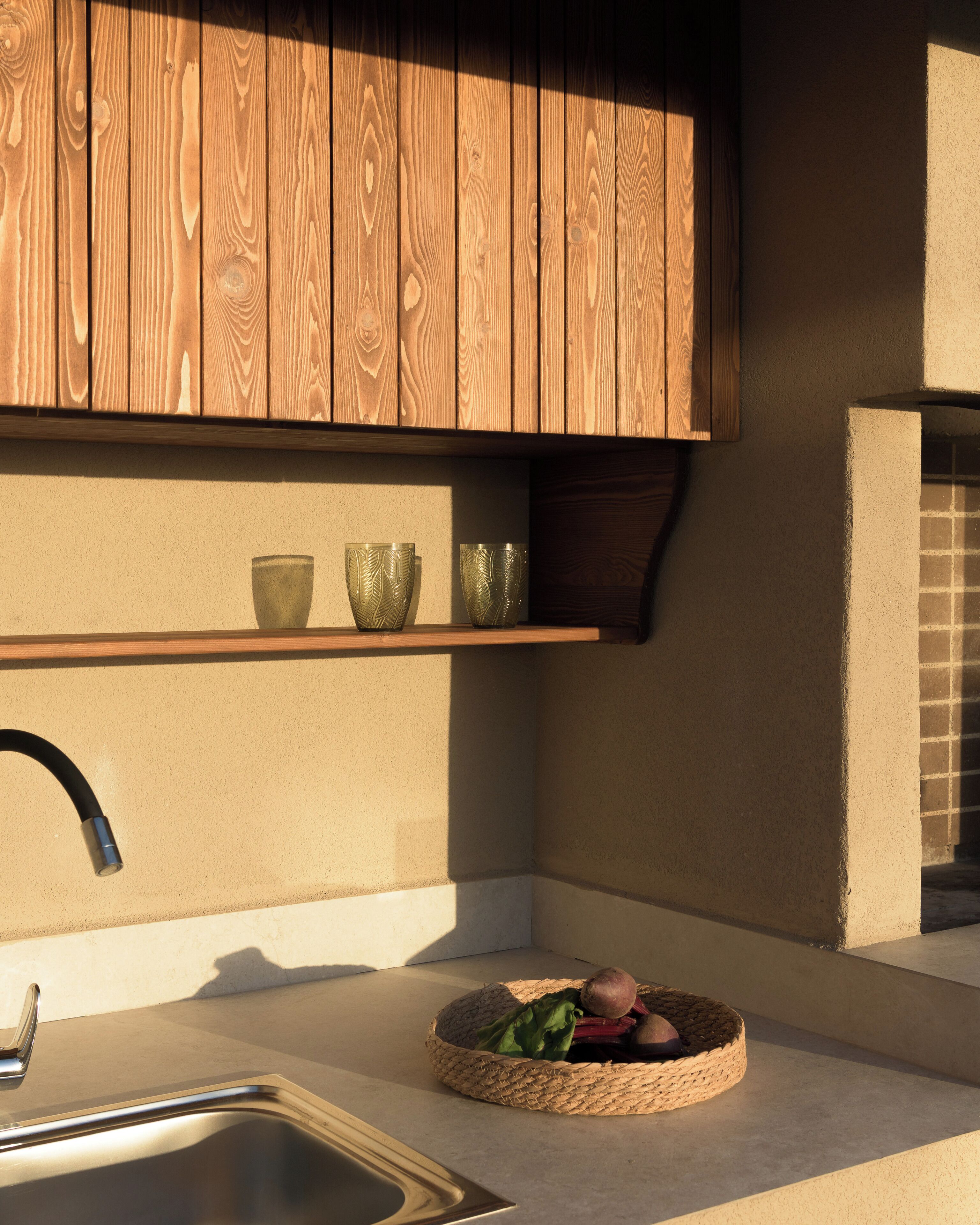 A kitchen with a wooden cabinet, a sink, and a woven basket with vegetables.