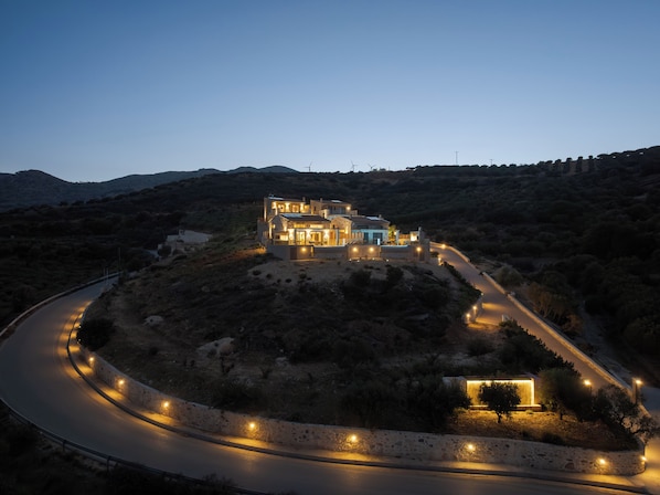 A modern house with a curved driveway, surrounded by hills and sparse vegetation. - Luxurious Stone Villas Crete (Malevizi)