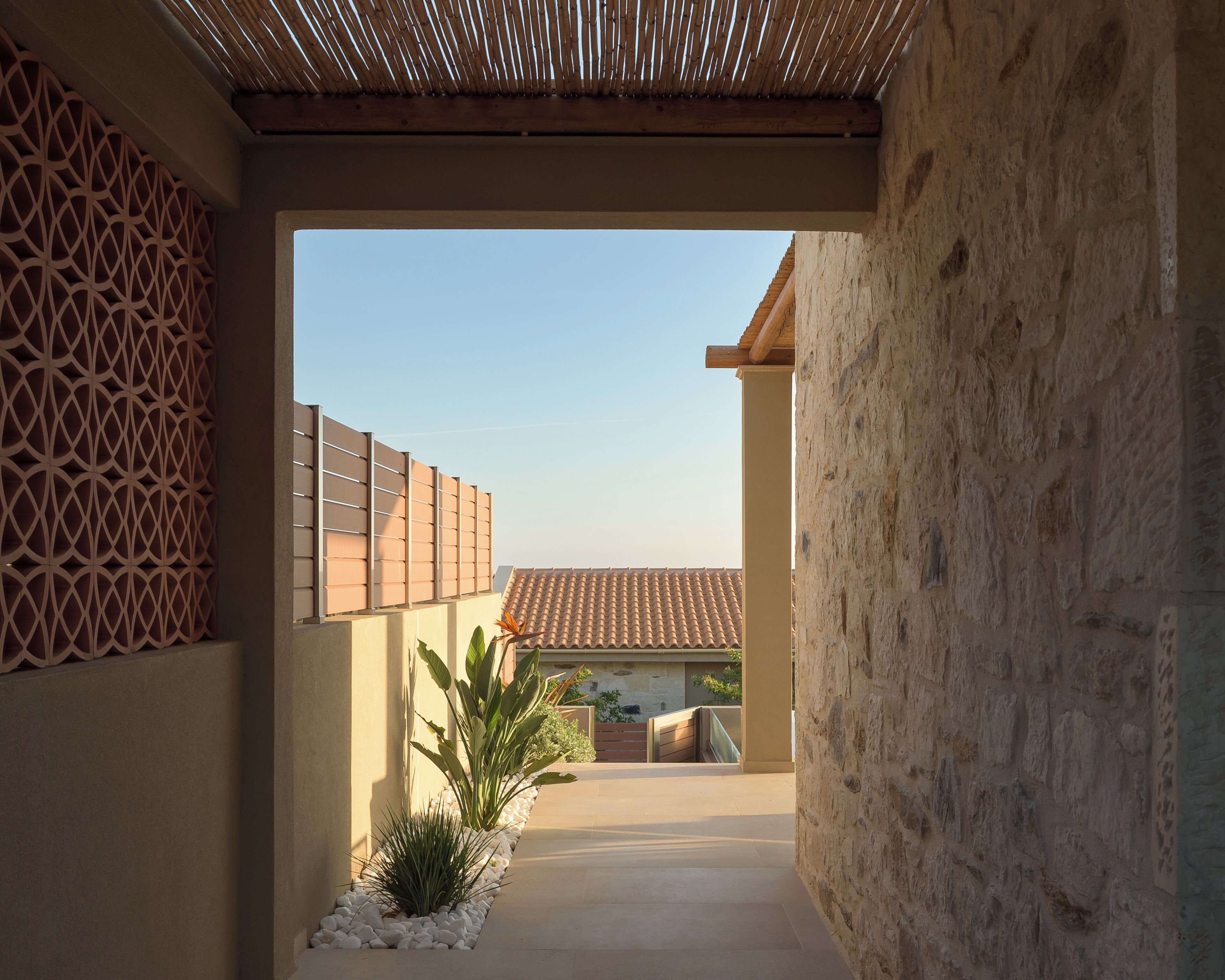 A corridor with a bamboo ceiling, stone walls, and a tiled roof visible through an archway.