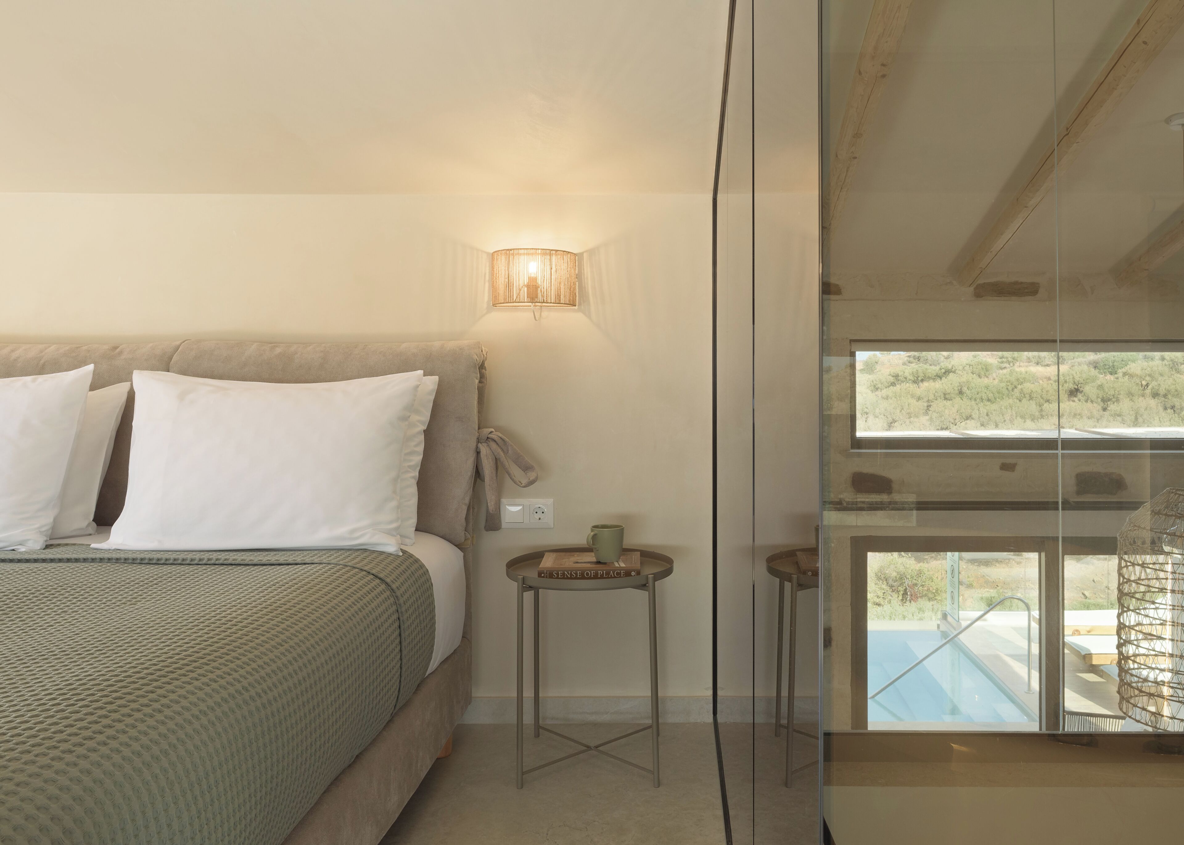 A bedroom with a bed, bedside lamp, nightstand, and a view of a pool through a glass door.