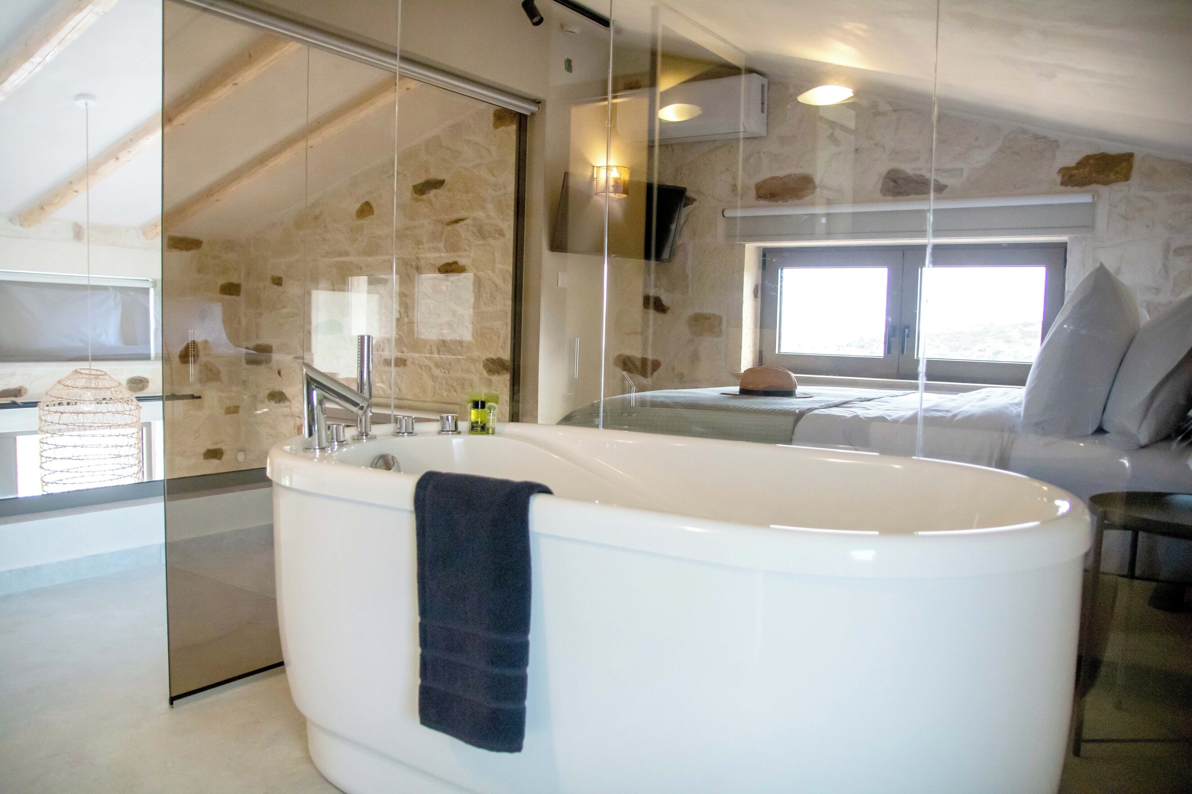 A modern bathroom with a freestanding bathtub, a glass shower enclosure, and a stone wall.