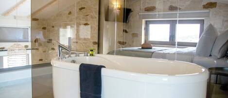 A modern bathroom with a freestanding bathtub, a glass shower enclosure, and a stone wall.