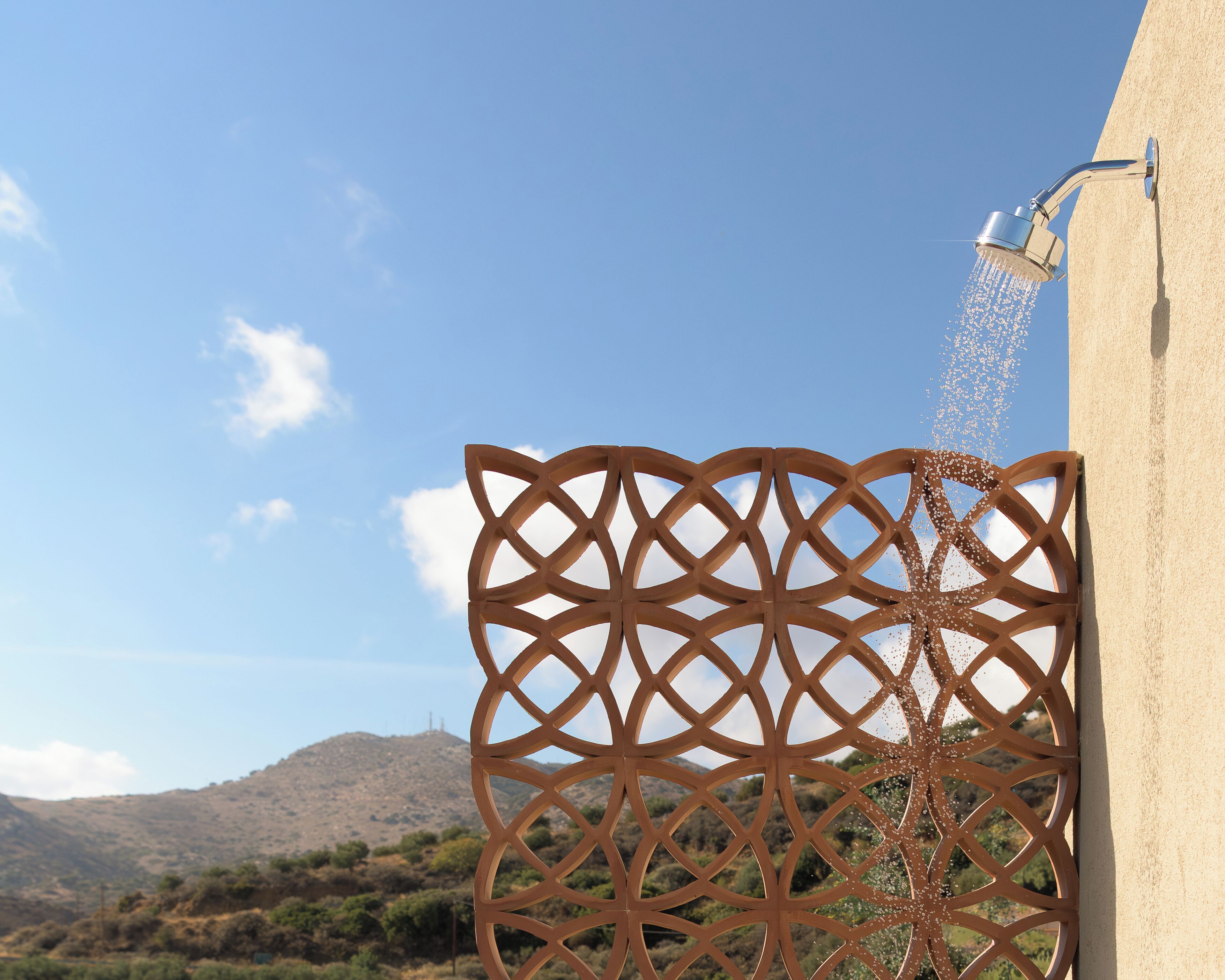 Une grille en métal ornée d’un motif géométrique, une fontaine et un paysage montagneux en arrière-plan.