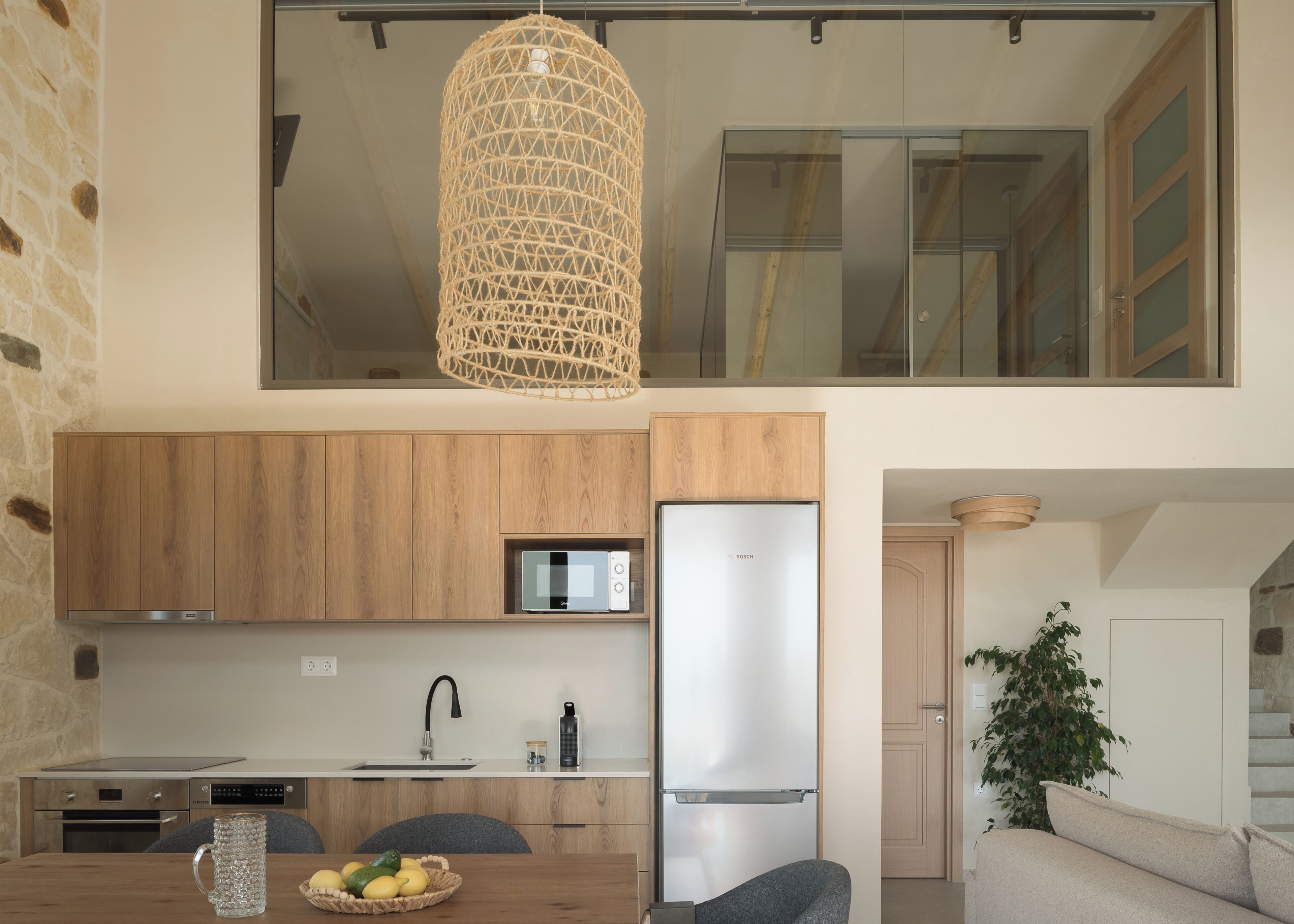 Een moderne keuken met houten kastjes, een Bosch koelkast, een magnetron en een hangende lamp.
