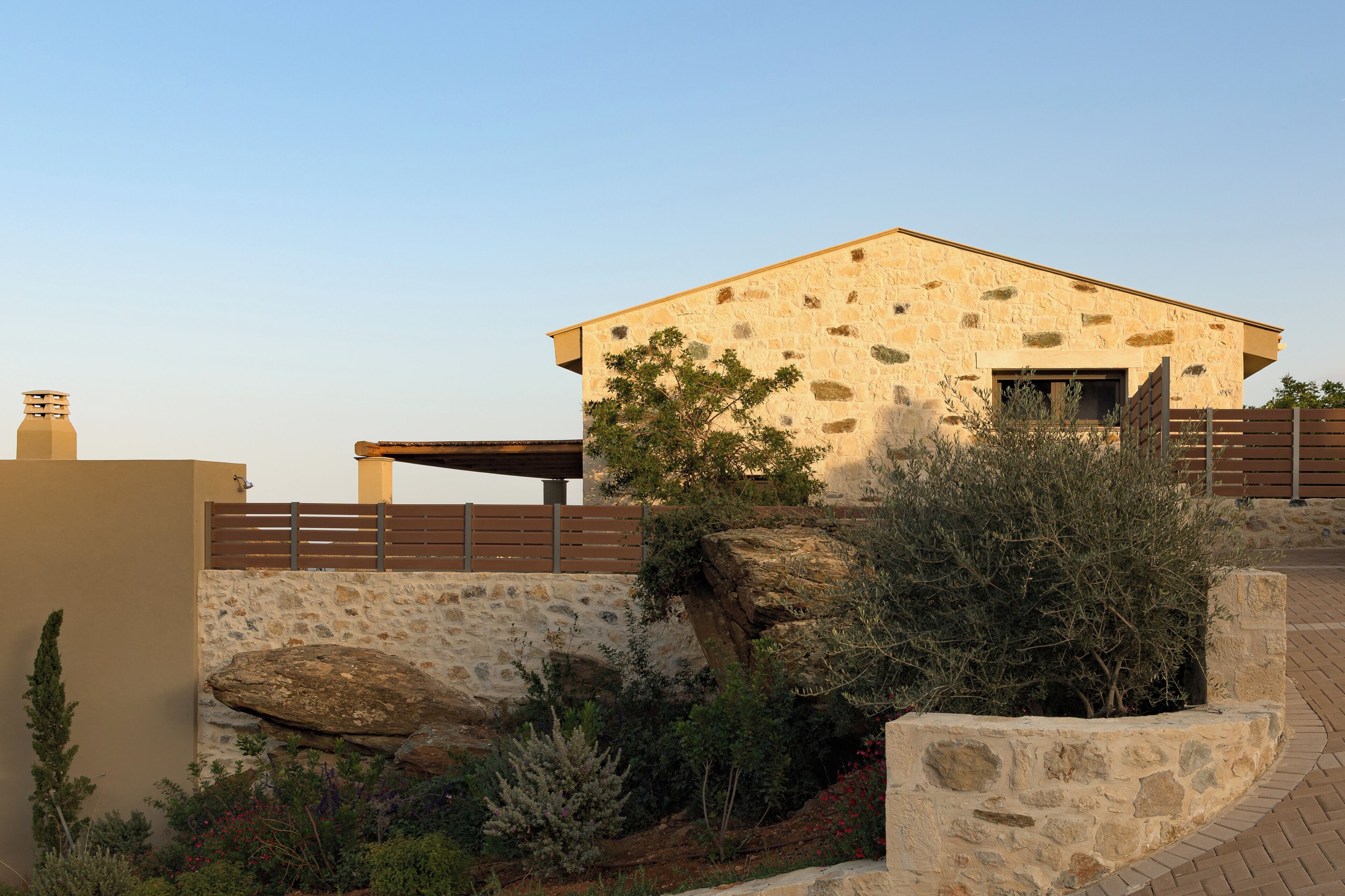 A stone building with a flat roof, a wooden fence, and a landscaped garden with rocks and shrubs.