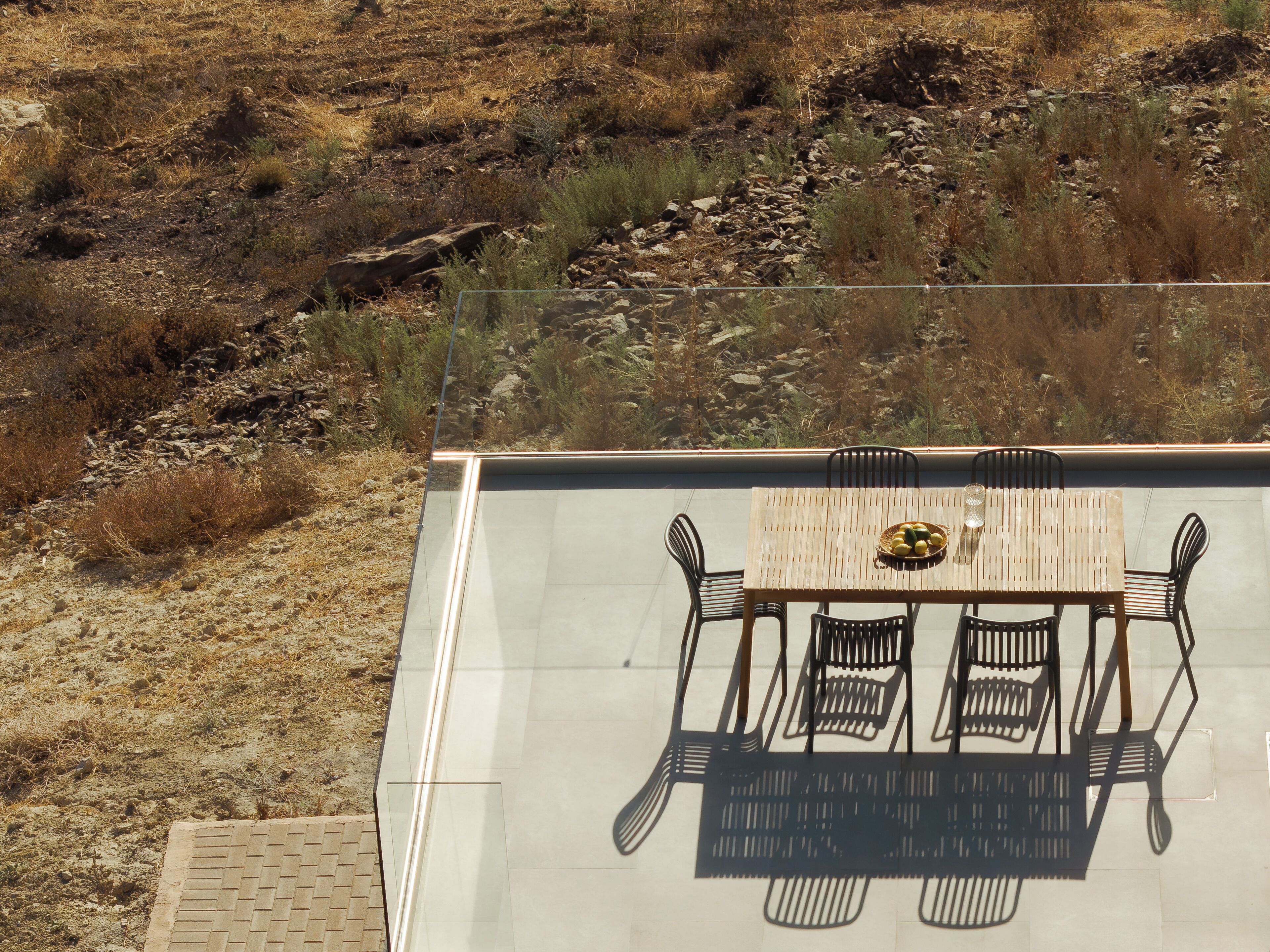 A dining area with a table and chairs, a glass partition, and a view of a dry, rocky landscape.